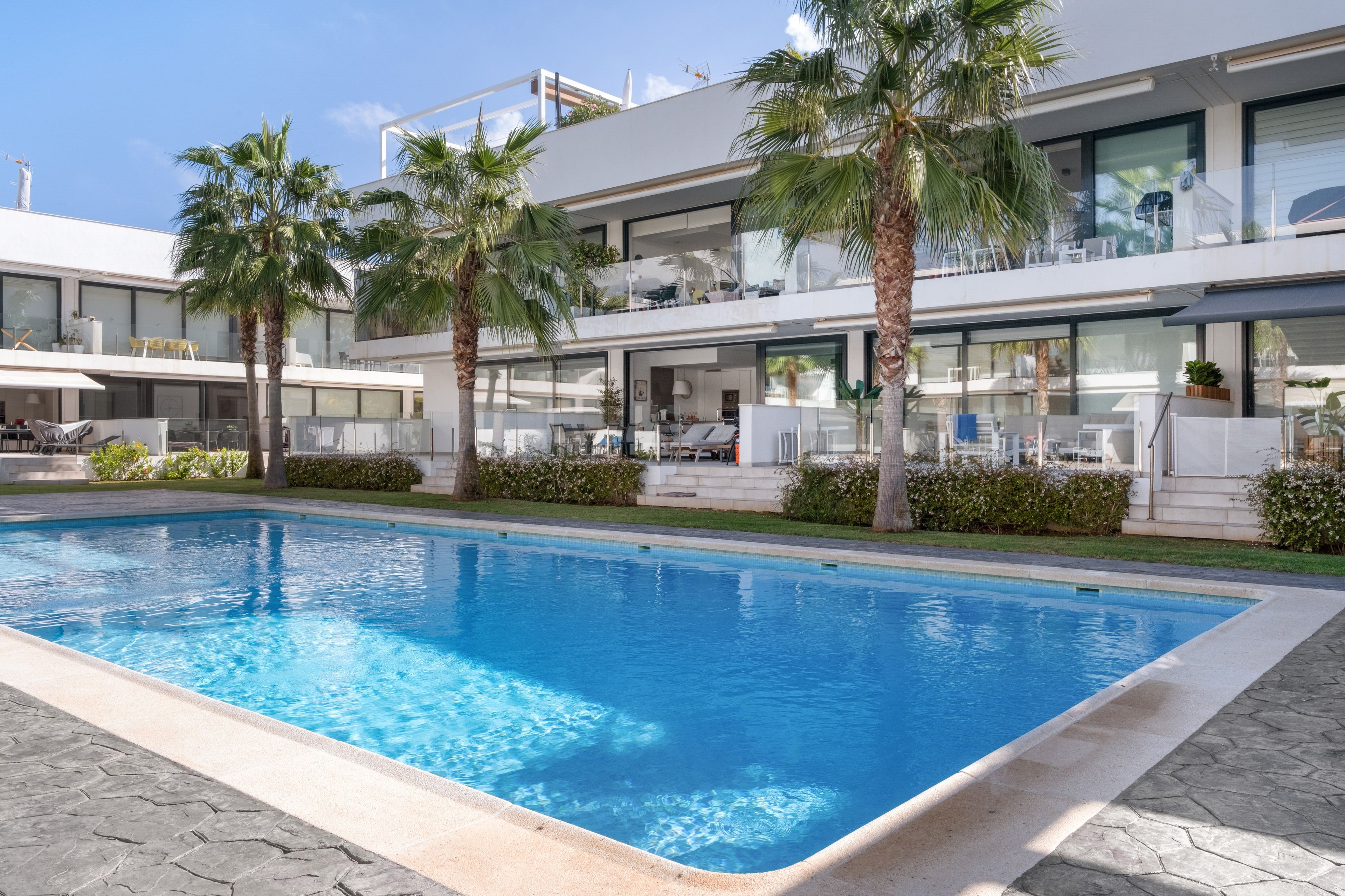 Un hotel moderno con piscina, palmeras y una estructura de dos pisos.