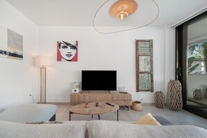 A modern living room with a flat-screen TV, a round wooden coffee table, a sofa, and a large window with a view of palm trees. - Holiday Home 'Tom 1 Hochwertiges Appartement' with Shared Pool, Wi-Fi and Air Conditioning (Mar de Cristal)