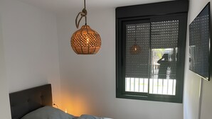 Une chambre à coucher avec un lit, un luminaire suspendu, une fenêtre avec des stores et un téléviseur fixé au mur.