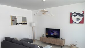 Un salon moderne avec un canapé, un téléviseur, une lampe sur pied et des œuvres d’art accrochées au mur.