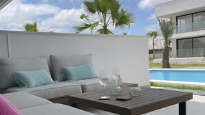 Un espace extérieur moderne, aménagé avec des sièges, une piscine, un mur blanc et un palmier.
