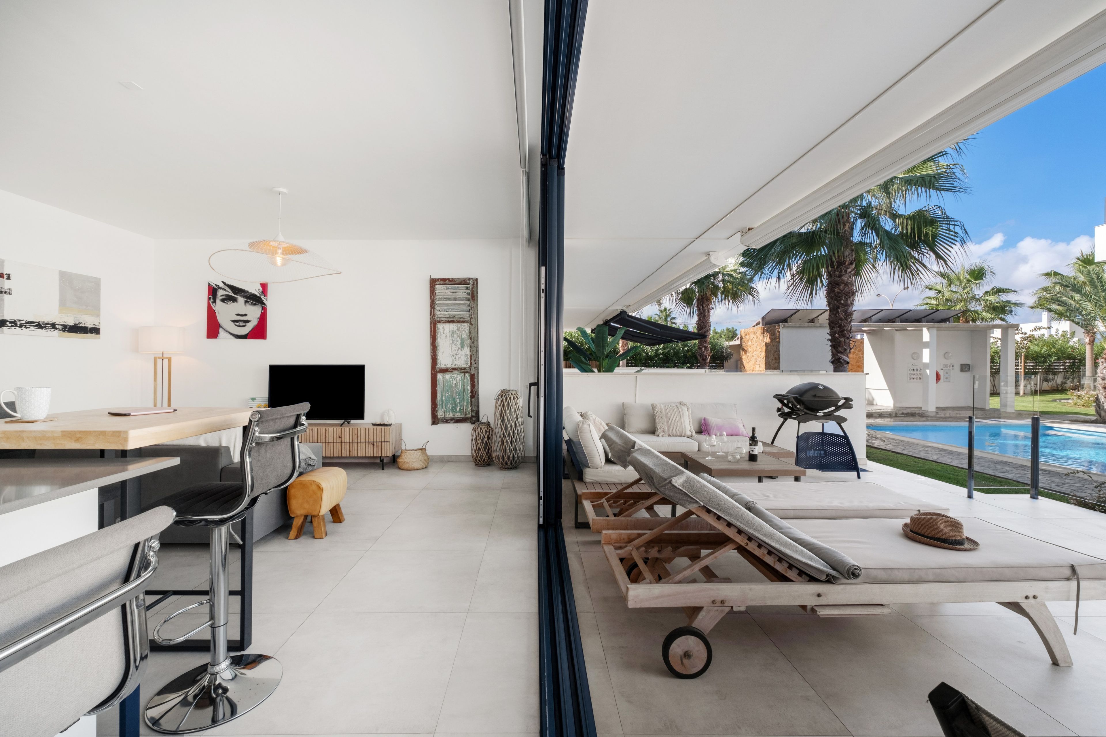 Una sala de estar moderna con televisor grande, comedor y vista a una piscina.