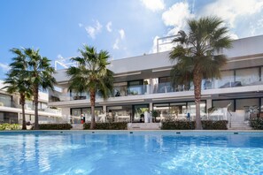 Un hotel moderno con piscina, palmeras y un cielo azul despejado.