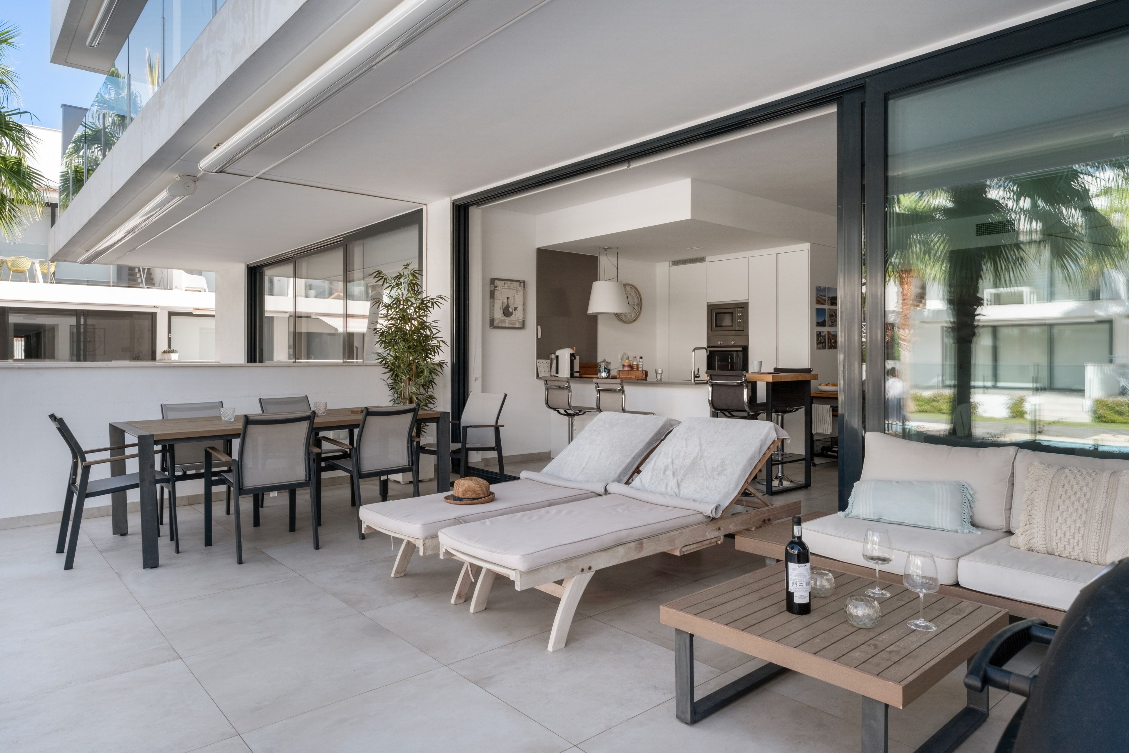 Un espace de vie extérieur moderne, doté d’une piscine, de chaises longues, d’une table à manger et d’une cuisine en arrière-plan.