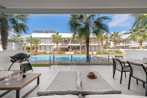 Un área de descanso exterior moderna con piscina, palmeras y vistas a un edificio contemporáneo.