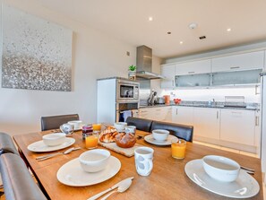 Eine moderne K üche mit Essbereich, ausgestattet mit einem Holztisch, der für das Frühstück gedeckt ist, einer Mikrowelle und einem Edelstahlbackofen.