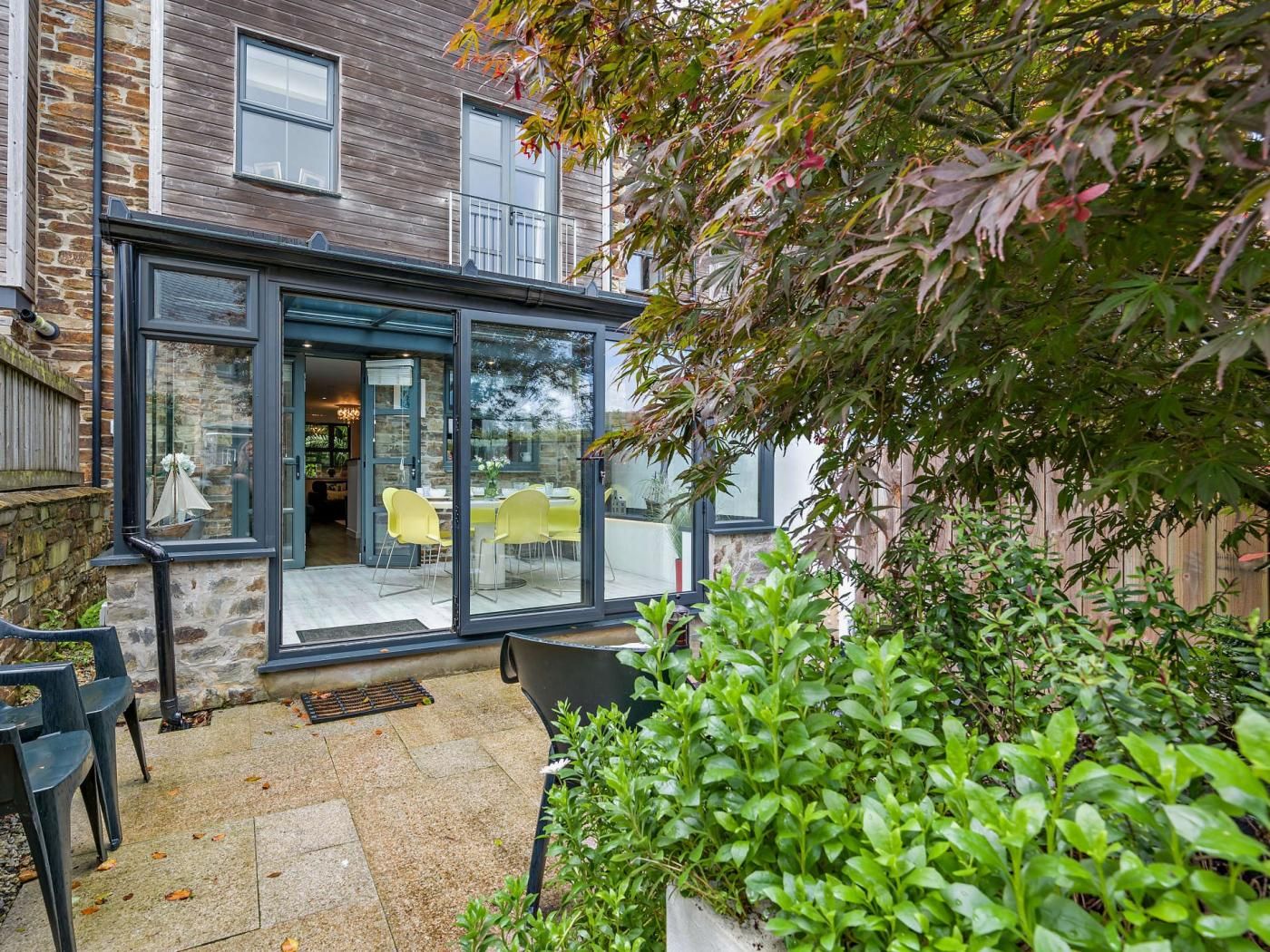 A modern building with a glass conservatory, stone walls, and a patio area with chairs and plants.