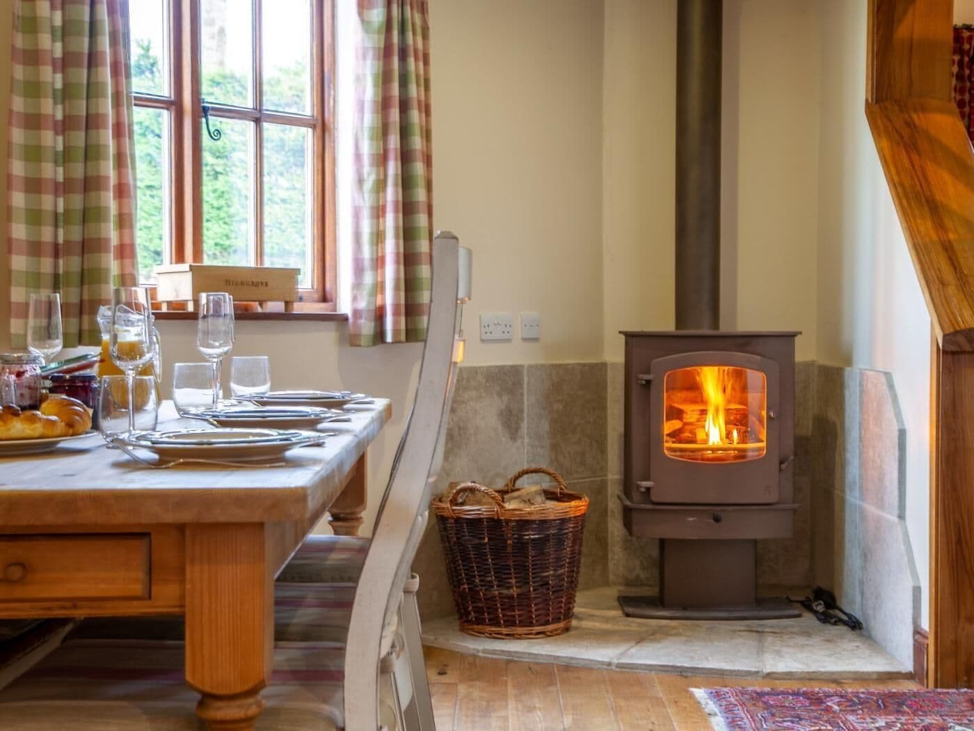 Un coin repas chaleureux avec une table mise pour le petit-déjeuner, un poêle à bois et une fenêtre avec des rideaux.