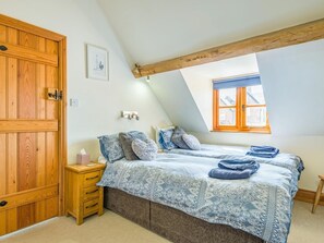 Ein Schlafzimmer mit Holztür, einem Nachttisch mit Taschentuchbox, einem Bett mit gemusterten Betttextilien und einem Fenster mit Aussicht.