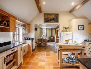 Eine Küche mit Holzausstattung, Fliesenboden, Essbereich mit Tisch und Stühlen, Kamin und einem Bild an der Wand.