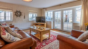 Ein Wohnzimmer mit einer Couch, Couchtisch, Fernseher und großen Fenstern.