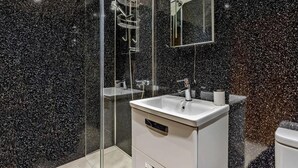 Ein modernes Badezimmer mit einer Glaskabine zur Dusche, einem weißen Waschbecken und einem Spiegel darüber.