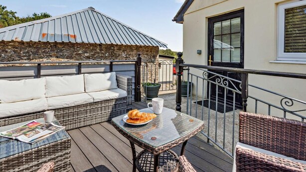 Ein Balkon mit einer Rattan-Couch, einem Tisch mit einem Croissant und einer Steinmauer.