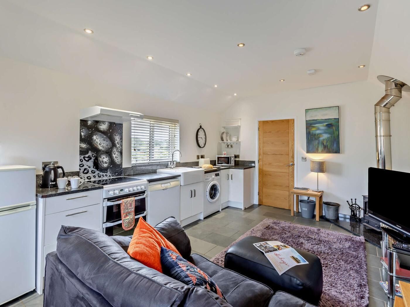 A compact living space with a kitchenette, a sofa, a flat-screen TV, and a painting on the wall.