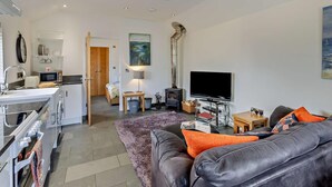 Ein modernes Wohnzimmer mit Ledersofa, Flachbildfernseher, Kamin und Küchenzeile mit Mikrowelle.