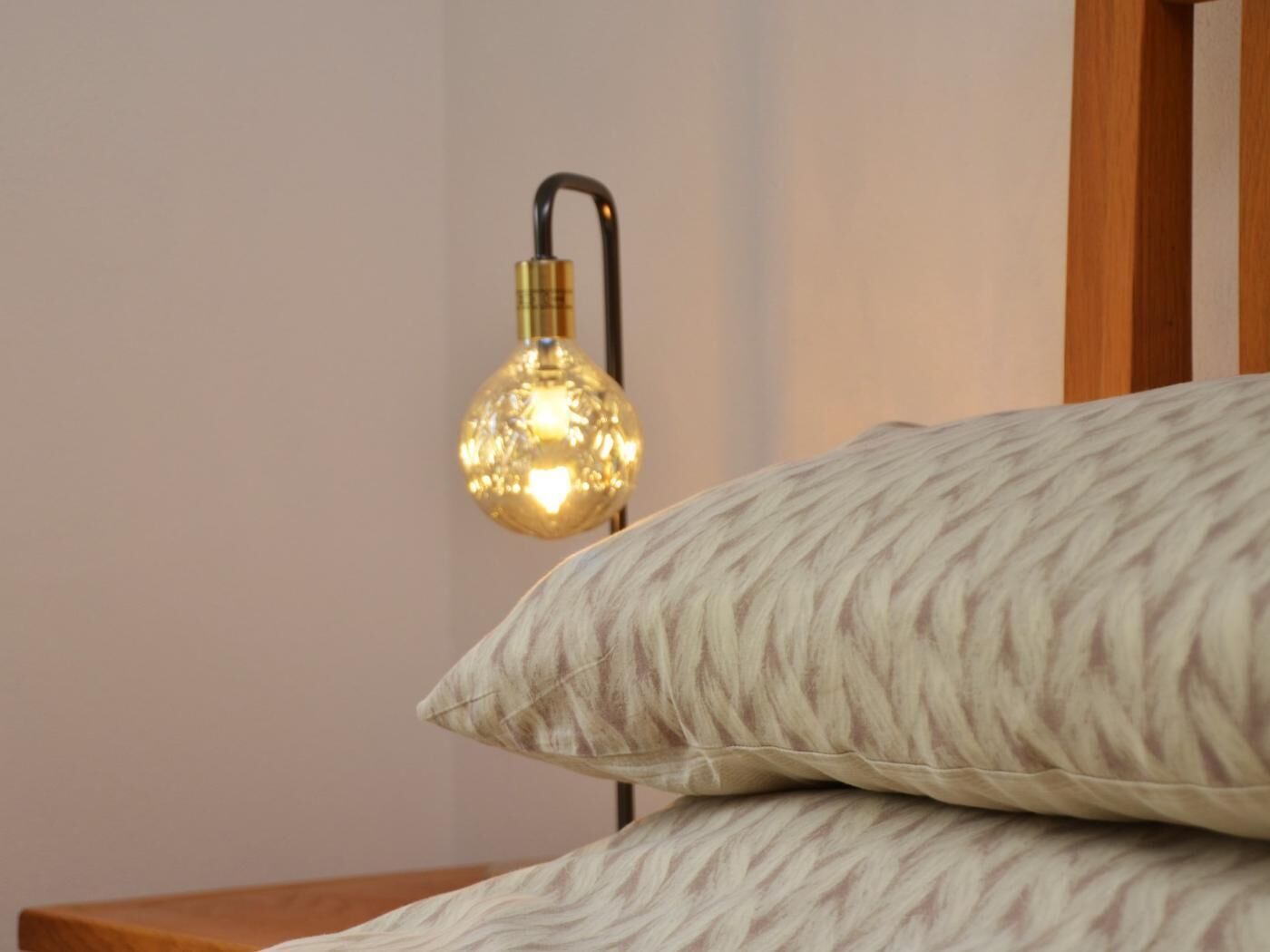 Ein Bett mit Holz-Kopfteil, einem strukturierten Kopfkissen und einer Wandleuchte.