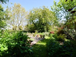 Ein Garten mit einer Terrassen-Sitzgruppe, umgeben von verschiedenen Pflanzen und Bäumen.