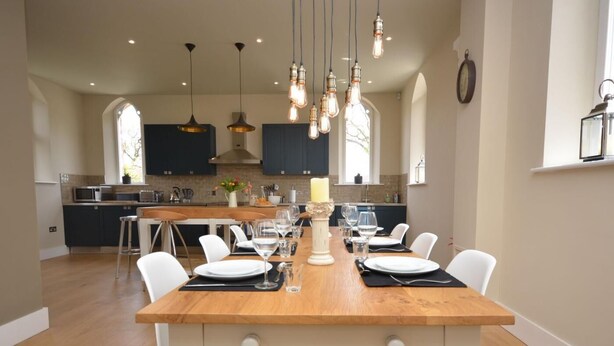 Comedor con mesa de madera, sillas blancas y lámparas colgantes.
