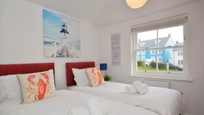 Una camera d'albergo con due letti, un quadro raffigurante un faro, una finestra vista case e un cartello appeso al muro.