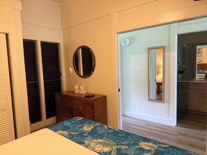 A bedroom with a bed, a dresser, a mirror, and a door leading to a bathroom. - Stunning Ocean View Condo on the beach w AC, Kiahuna Plantation, Poipu Beach (Koloa)