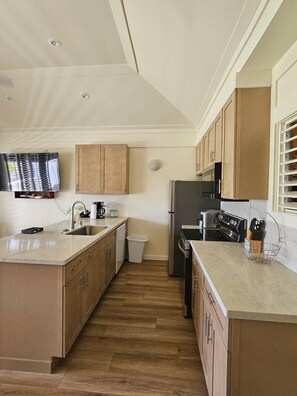 A modern kitchen with wooden cabinets, stainless steel appliances, and a large island with a sink. - Stunning Ocean View Condo on the beach w AC, Kiahuna Plantation, Poipu Beach (Koloa)