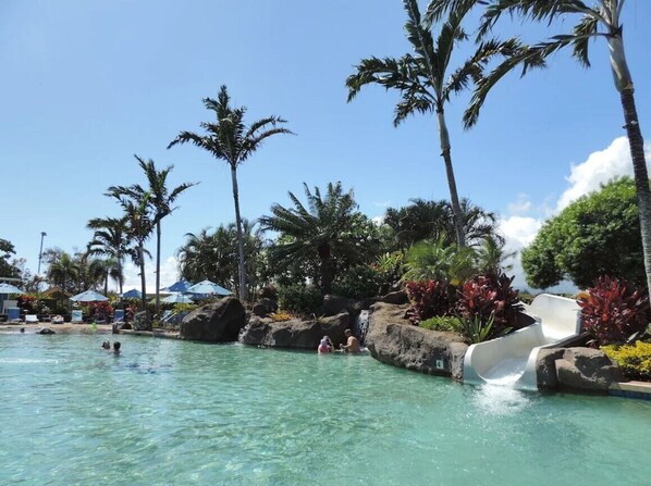 Ein Poolbereich mit klarem Wasser, Palmen und einer Wasserrutsche.