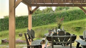 A wooden gazebo with a table and chairs, a guitar, and a bottle of wine. - 2 Bed in Crickhowell (oc-42920) (Llangattock)