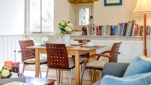 A dining area with a table set for four, surrounded by chairs, a bookshelf with books, and a window with a view. - 2 Bed in Crickhowell (oc-42920) (Llangattock)