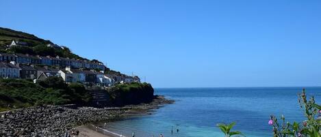 A coastal town with houses on a hillside, a rocky beach, and clear blue water.
