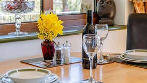Uma mesa de jantar posta com pratos, copos, uma garrafa de vinho, um vaso com flores amarelas e saleiro e pimenteiro.