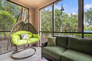 A hanging chair with cushions and a sofa with pillows, both facing a large window with a view of trees and a street lamp outside. - Galactic Oasis in Kissimmee (Davenport)