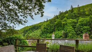 A wooden table with a teapot, a mug, and a map, surrounded by chairs, overlooking a lush green hillside. - 3 Bed in Minehead (oc-44078) (Porlock)
