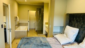 A bedroom with a bed, a dark headboard, and a bathroom with a bathtub and shower. - Cozy 1-bedroom apartment in superb Pretoria with gym, pool (Pretoria)