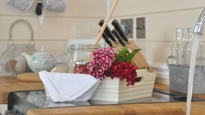Una encimera de cocina con un hervidor, un frasco, un bloque de cuchillos y un arreglo floral.