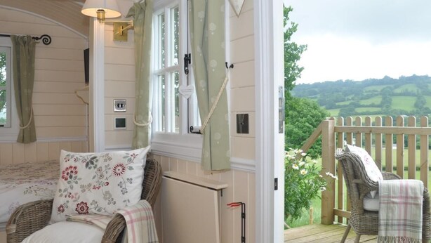 Una habitación con cama, una silla de mimbre, vistas al campo y una terraza de madera.