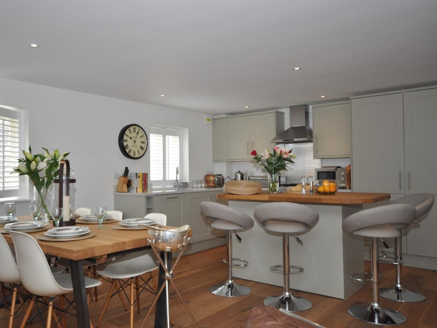 Una cocina moderna con comedor, que incluye una mesa de madera, sillas blancas y un taburete de bar.