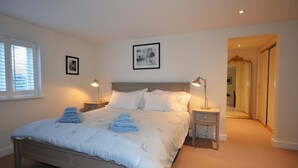 Un dormitorio con una cama, dos mesitas de noche, una ventana y una puerta que da a otra habitación.