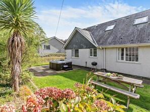 Ein Haus mit Whirlpool, Grill und Picknicktisch im Garten.