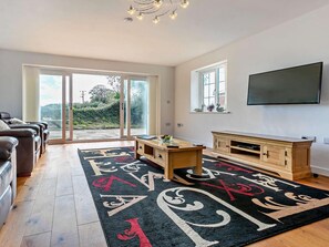 Ein geräumiges Wohnzimmer mit einem großen Schiebeglasfenster zum Garten, einem Holz-Fernsehschrank und einem schwarz-roten Teppich.