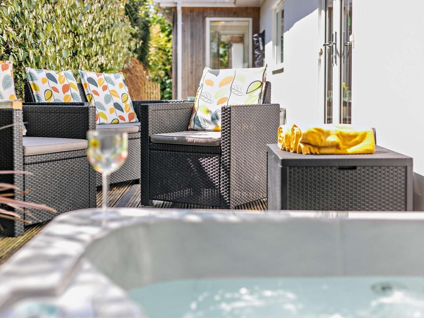 A patio area with wicker furniture, a hot tub, and a glass table.
