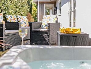 A patio area with wicker furniture, a hot tub, and a glass table. - 2 Bed in Newquay (oc-44953) (Cubert)