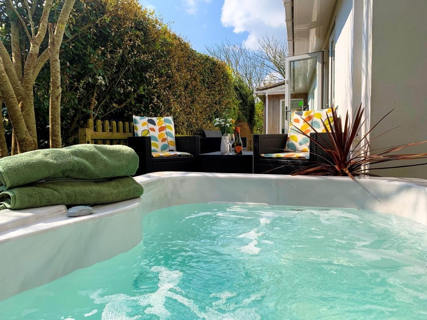 Ein Whirlpool mit freiem Blick auf den Himmel, umgeben von Grünpflanzen und Gartenmöbeln.