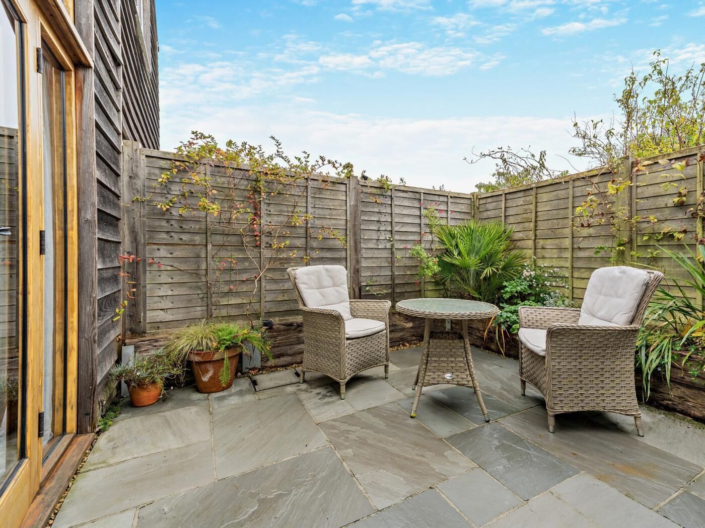 Une terrasse dotée de meubles en osier, d’une table ronde et de plantes en pot.