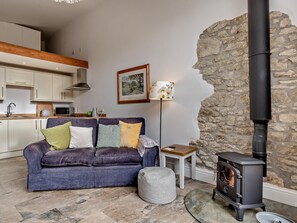 A cozy living room with a sofa, a small table, a lamp, a stone wall, and a wood-burning stove. - 1 Bed in Gillingham (oc-46774) (Bourton)