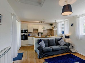 Eine moderne Küche mit weißen Schränken, einem eingebauten Backofen und einem Essbereich mit grauem Sofa und gemusterten Kissen.