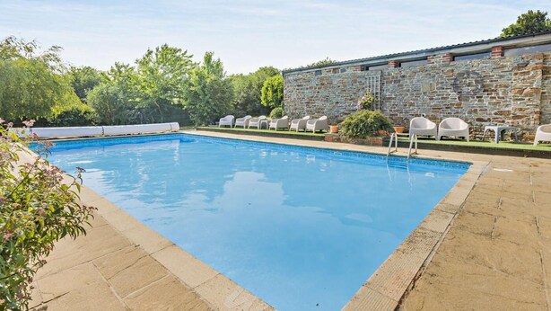 Ein rechteckiger Pool mit einer Steinmauer und weißen Liegestühlen.