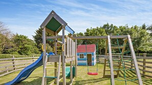 Ein Spielplatz aus Holz mit Rutsche, Schaukel und Klettergerüst.