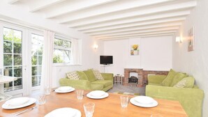Ein Essbereich mit einem Holztisch, gedeckt für vier Personen, einer grünen Couch, einem Fernseher und einem Kamin.