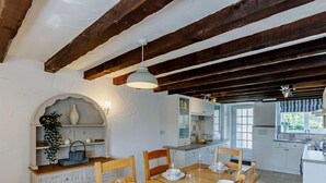 Un coin repas avec une table en bois dressée pour quatre personnes, des meubles blancs et une cuisine en arrière-plan.