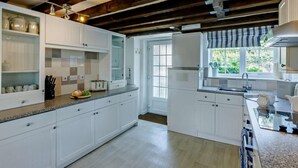 Une cuisine moderne avec des meubles blancs, un four encastré et une fenêtre donnant sur un paysage verdoyant.